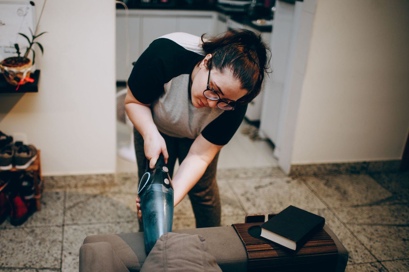 An adult woman vacuuming in a cozy living room with books on the sofa in a modern apartment.
